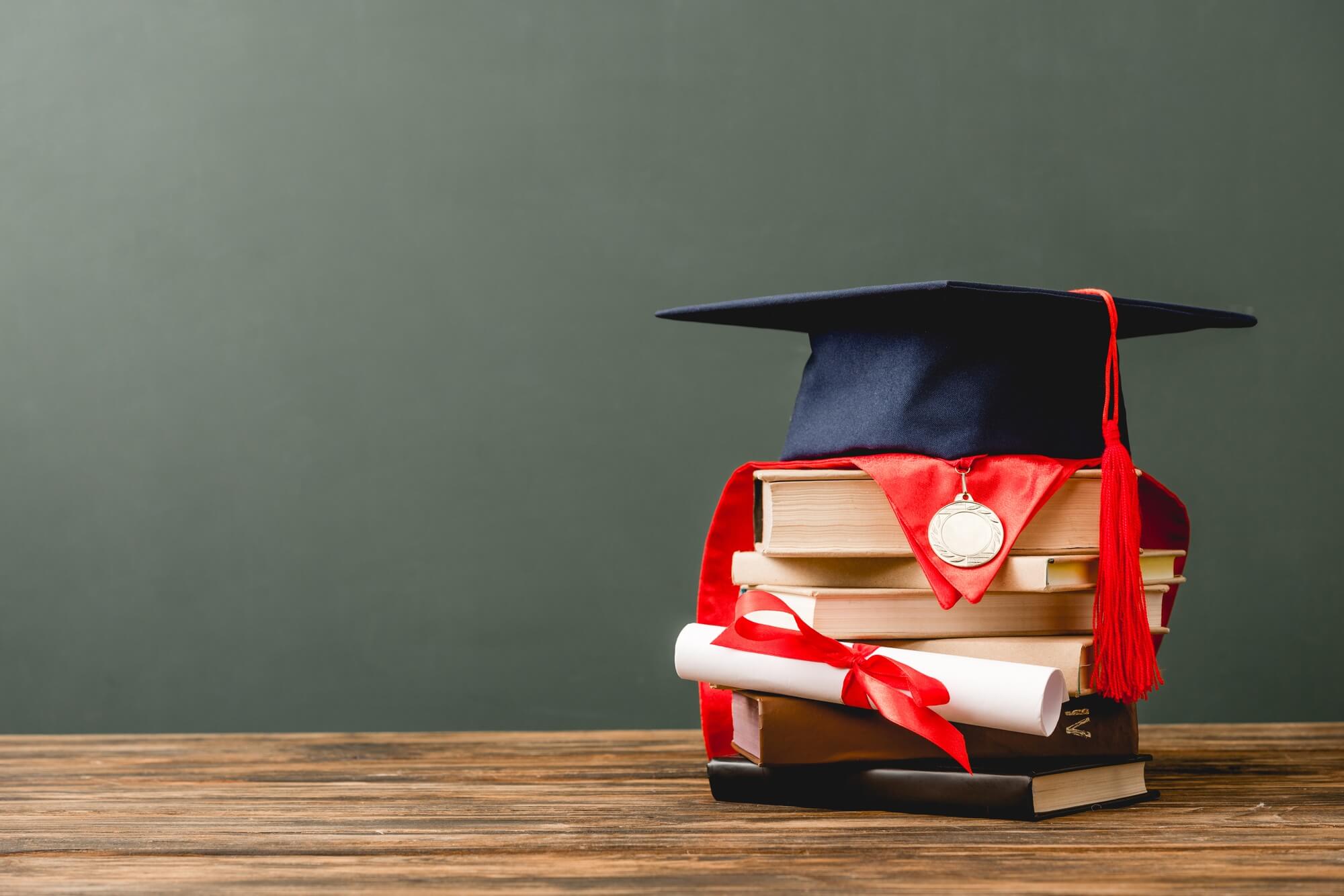 books, academic cap, medal and diploma on wooden surface isolated on grey